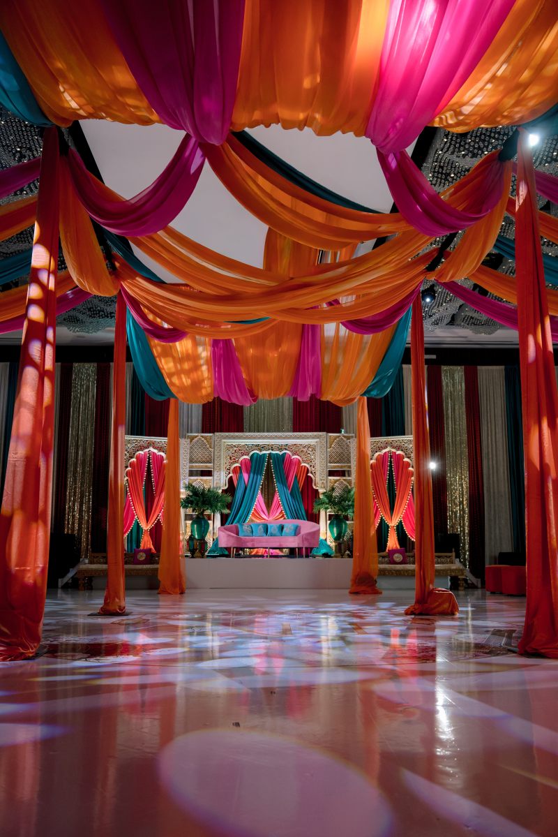 Wide view of a sangeet ballroom with colourful ceiling draping over the dance floor by GPS Decors