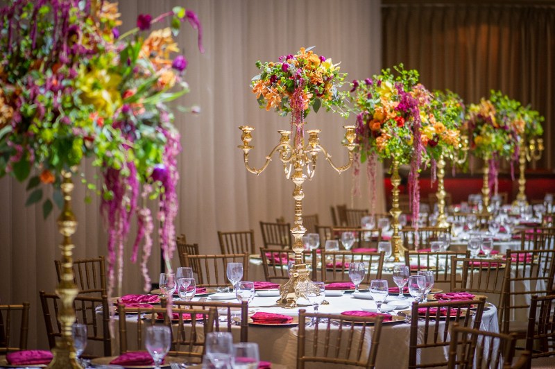 Tall gold candelabra centrepiece with orange and pink florals over mehndi tables by GPS Decors