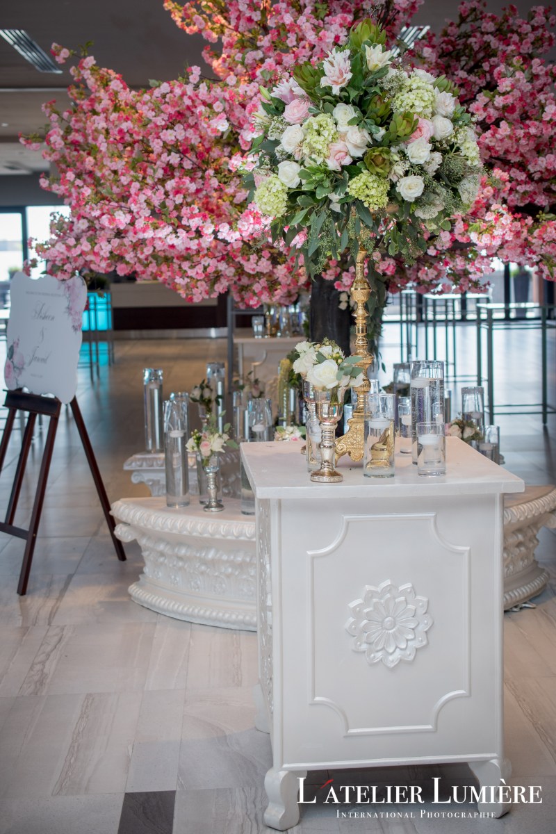 Pink cherry blossom trees behind a white floral pedestal at a reception by GPS Decors