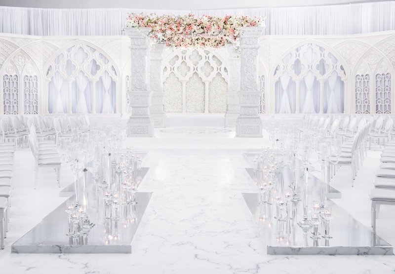 All-white wedding aisle leading to a floral stage by GPS Decors