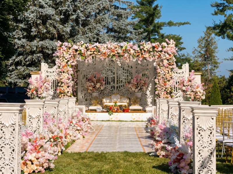 Outdoor mandap with a pink floral canopy, white carved panels and a floral-lined aisle at Terrace on the Green by GPS Decors
