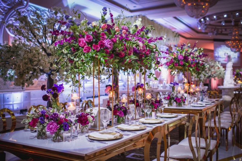 Reception tables with tall purple and pink floral centrepieces and candlelight at Bellvue Manor by GPS Decors