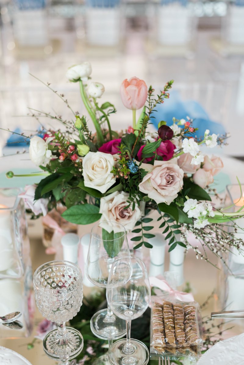 Low centrepiece of blush roses, pink tulips and greenery beside crystal glassware by GPS Decors
