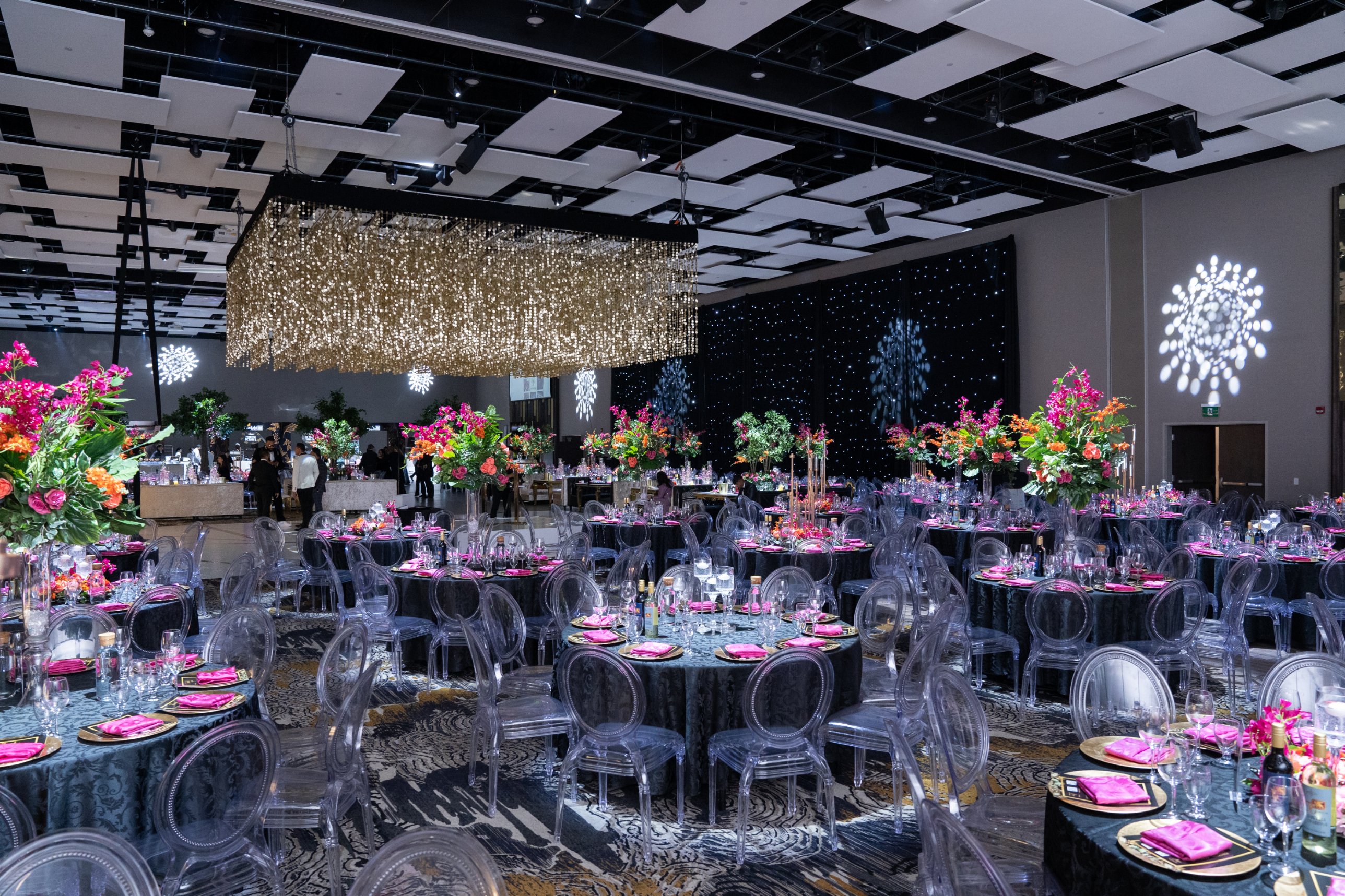 Wedding reception at Queen's Manor Event Centre in Brampton with a gold crystal chandelier, tall pink and orange floral centrepieces and a starlight backdrop by GPS Decors