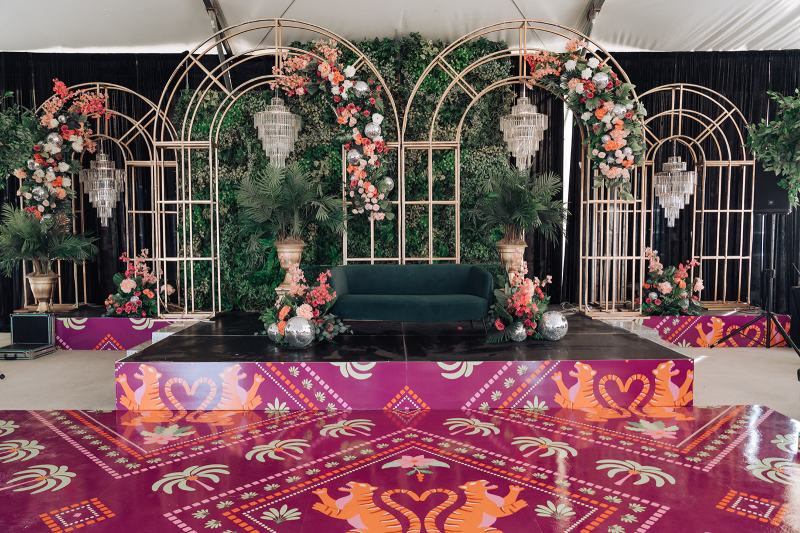 Sangeet stage with arched mirror panels, florals, green velvet sofa and pink printed dance floor by GPS Decors