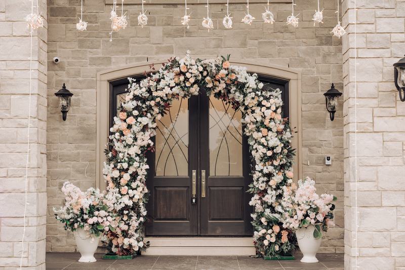 White and blush floral arch framing double front doors on the wedding morning by GPS Decors