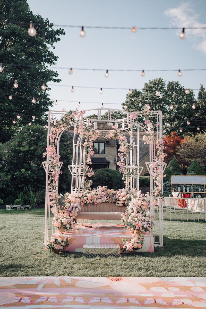Outdoor mehndi stage with a white frame wrapped in pink florals by GPS Decors