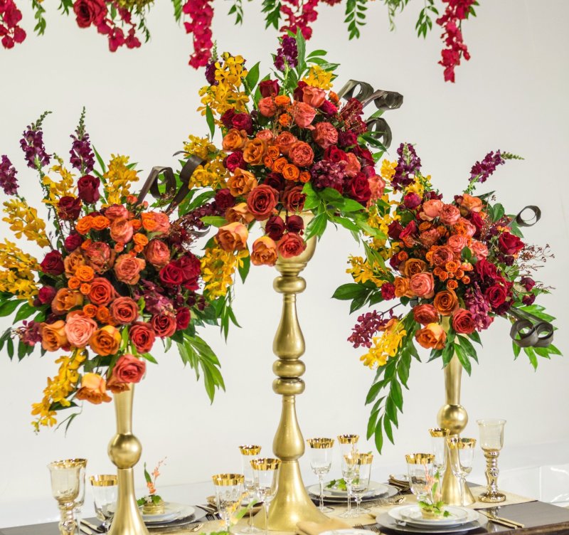 Close view of orange and red rose arrangements on tall gold vases by GPS Decors