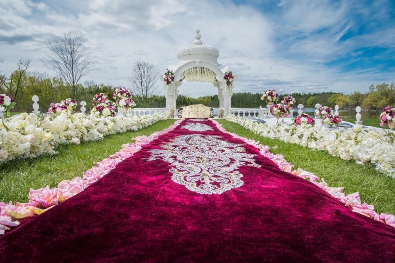 Outdoor wedding ceremony with a white gazebo and ornate red carpet aisle by GPS Decors