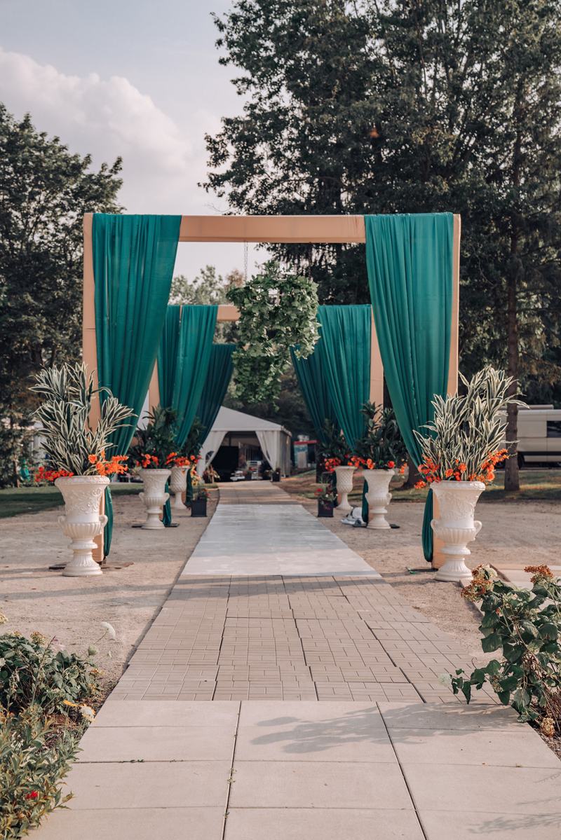 Outdoor aisle lined with teal draped frames and white urns by GPS Decors