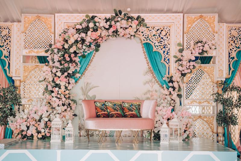 Stage with pink floral arch, teal drapes and blush sofa by GPS Decors