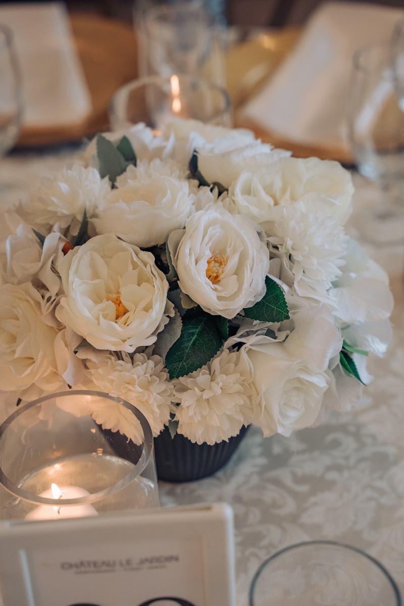 Low white rose centrepiece with candles on a reception table by GPS Decors