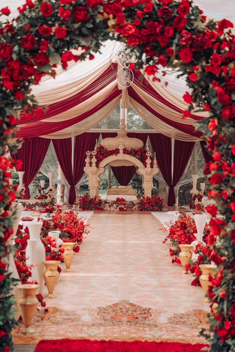 Red rose arch framing a burgundy draped tent and carved palki for an Anand Karaj by GPS Decors
