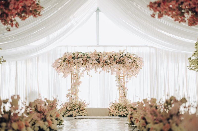 Blush floral canopy over a gold-frame palki in a white draped tent.