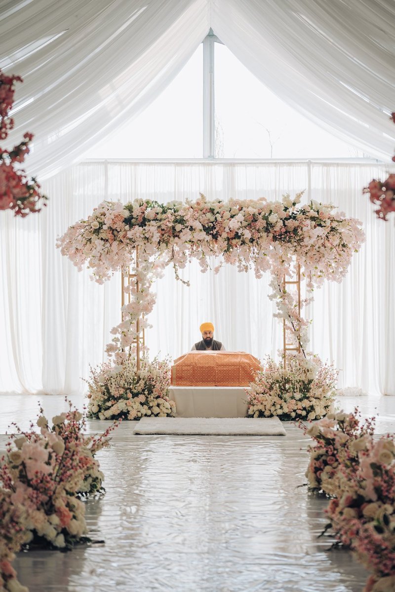 Blush floral palki at the end of a mirrored aisle in a white draped tent.