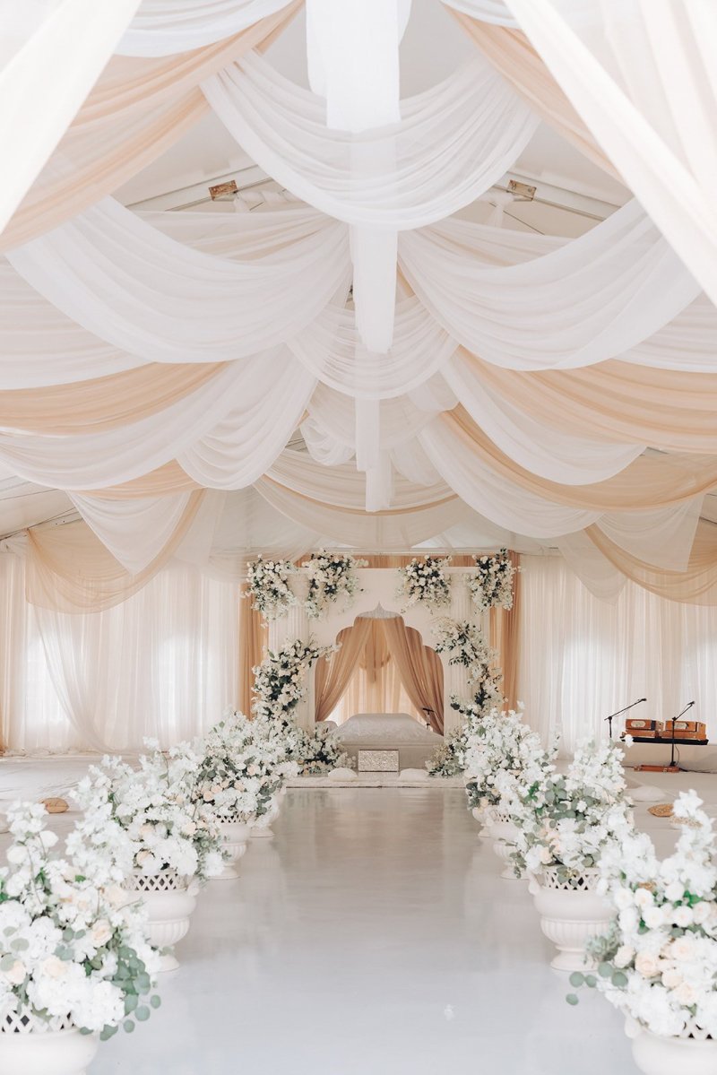 Draped white and peach tent ceiling over a white floral aisle leading to the palki.