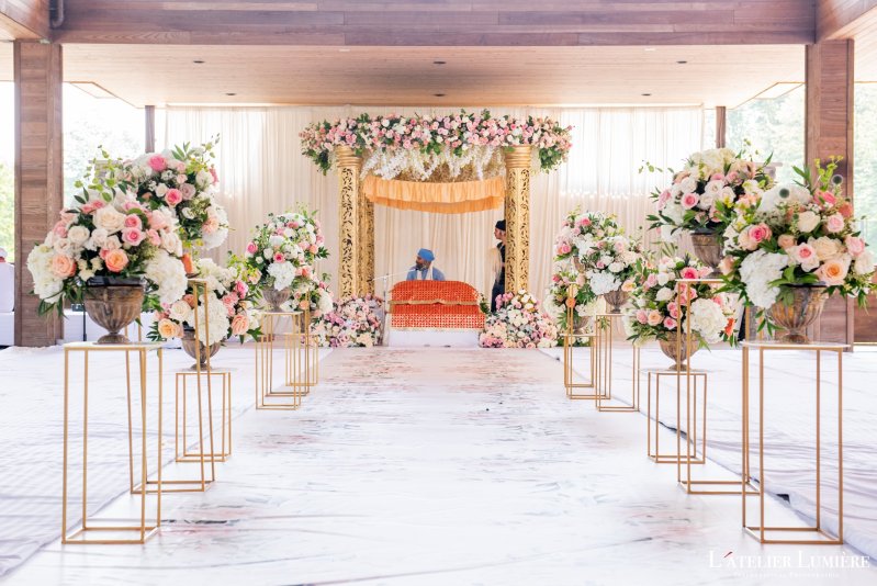 Gold-pillar palki with a pink floral canopy at the end of an aisle lined with floral arrangements on gold stands.