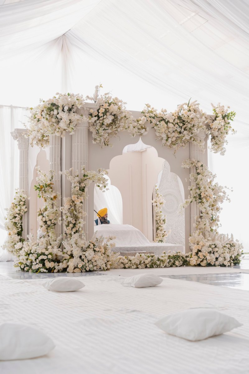 White jali palki structure dressed in white florals inside a white tent, with floor cushions for guests.