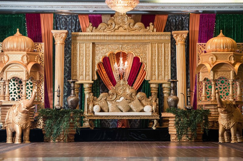 Gold palace-style stage with domed pavilions, gold elephant statues, jewel-tone drapes and an ornate gold sofa.