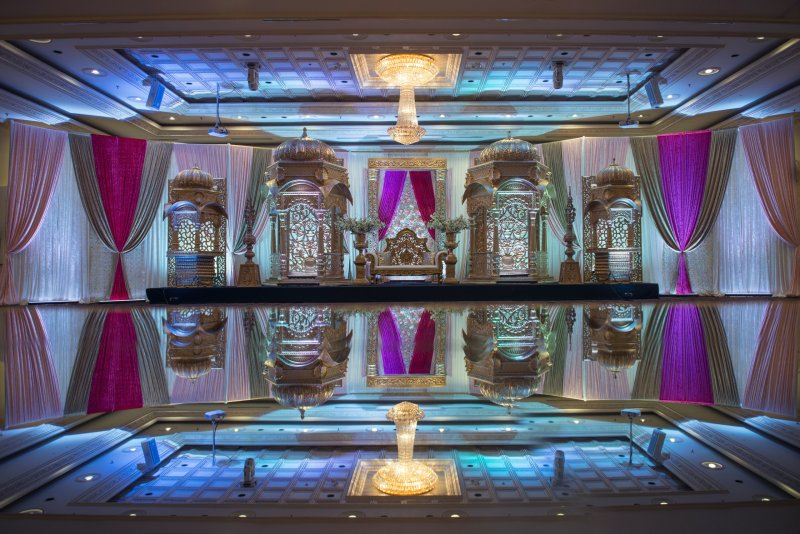 Ballroom stage with silver carved domed pavilions, magenta drapes and a throne seat reflected in a glossy floor.