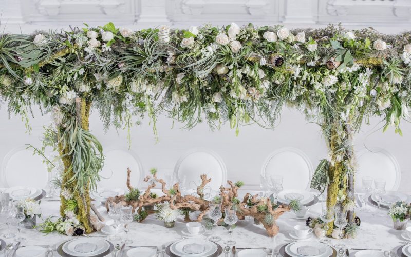 Greenery and air-plant arch over a long dining table with driftwood accents.