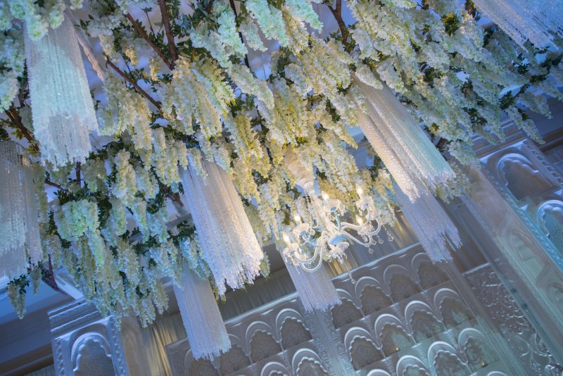 Close-up of hanging white wisteria and crystal strands above carved white panels.