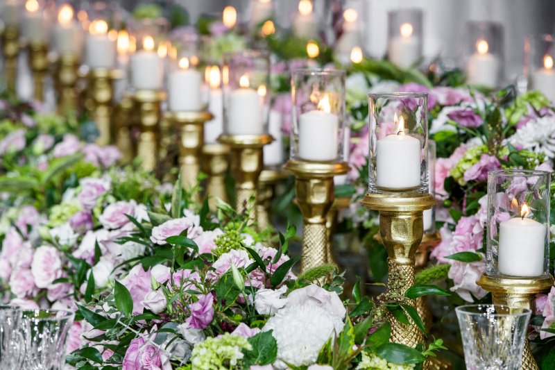 Close-up of a lavender and white floral runner with gold candlesticks and glass hurricane candles.