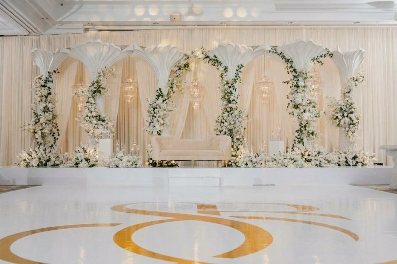 White calla lily arch stage with greenery and a gold monogram dance floor at Embassy Grand Convention Centre by GPS Decors
