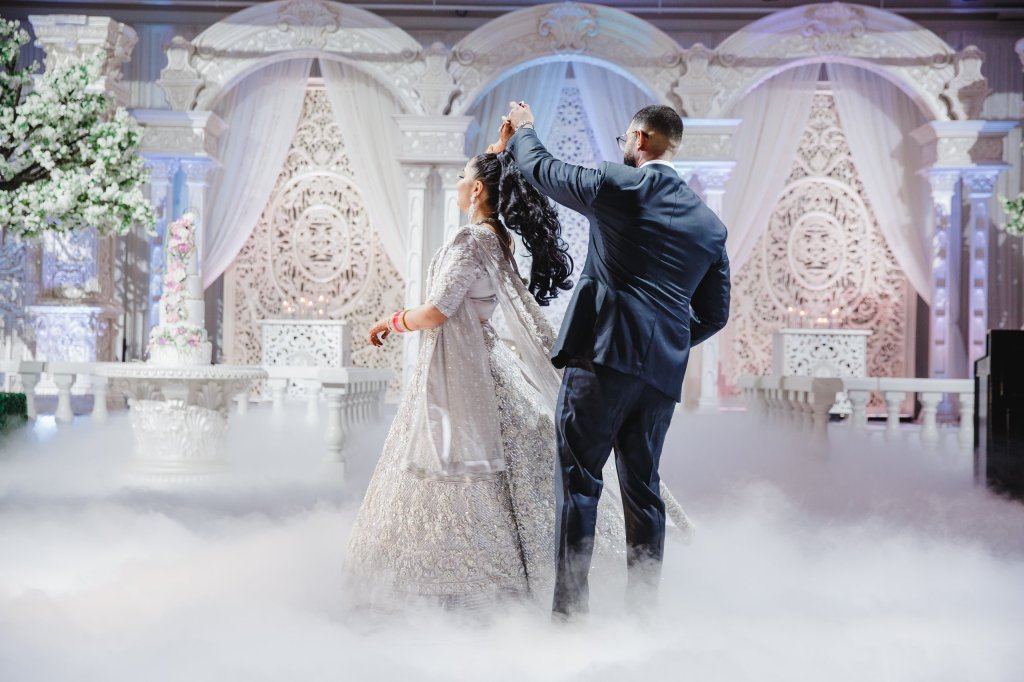 Couple dancing on a cloud-effect dance floor in front of a white carved arch stage with blossom trees.