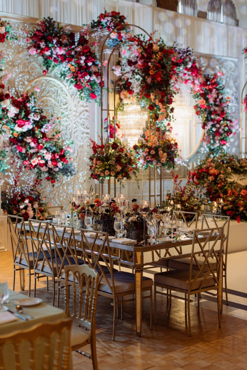 Red and pink floral ring stage behind a gold mirrored dining table with gold chairs.