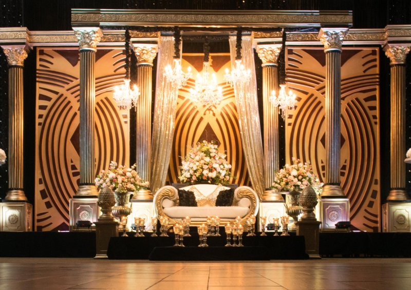 Gold art deco stage with columns, crystal chandeliers, sparkling drapes and a gold loveseat with florals.