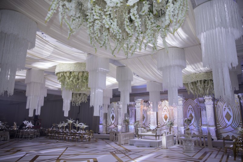 White draped ceiling with hanging white floral and crystal chandeliers above a white carved stage and geometric dance floor.