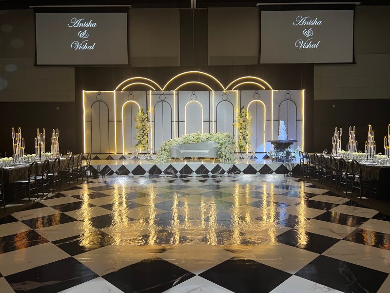 Reception with an illuminated arch stage, white florals and a loveseat, black-and-white checkered dance floor and tall candelabra centerpieces.