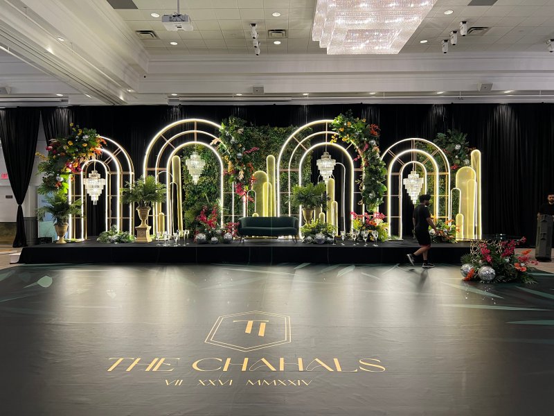 Reception stage with illuminated arch frames, greenery and tropical florals and crystal chandeliers above a custom-printed dance floor.
