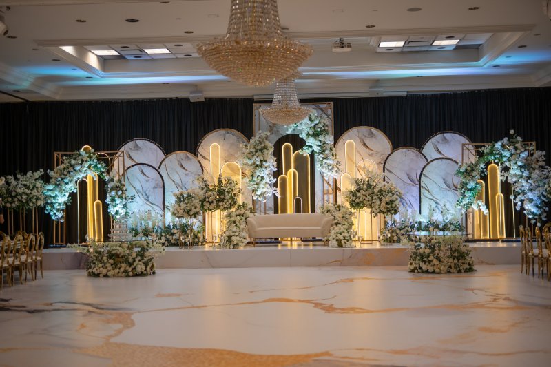 Marble-look arch stage with gold-lit arches, white florals and a sofa above a gold-veined dance floor.