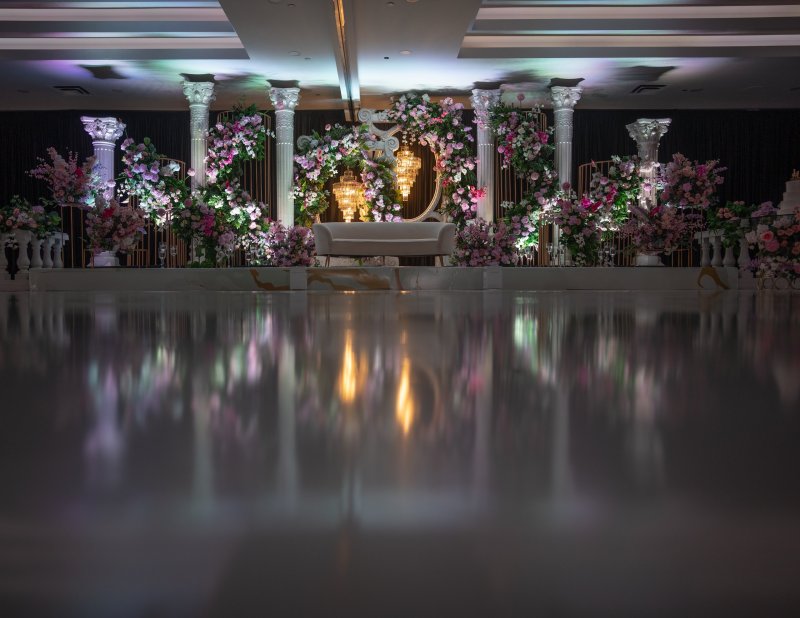 White column stage with pink and lavender florals, gold arches and a white sofa, seen from dance floor level.