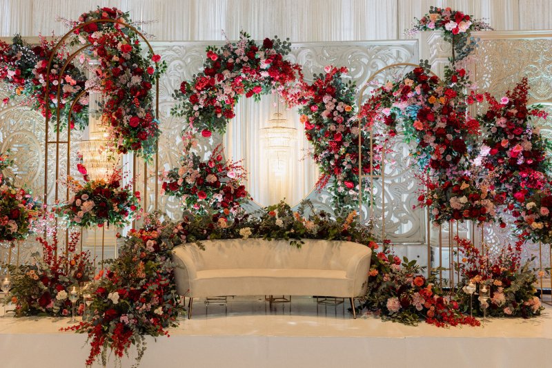 Stage with gold arches and floral rings in red, pink and burgundy blooms around a cream curved sofa.