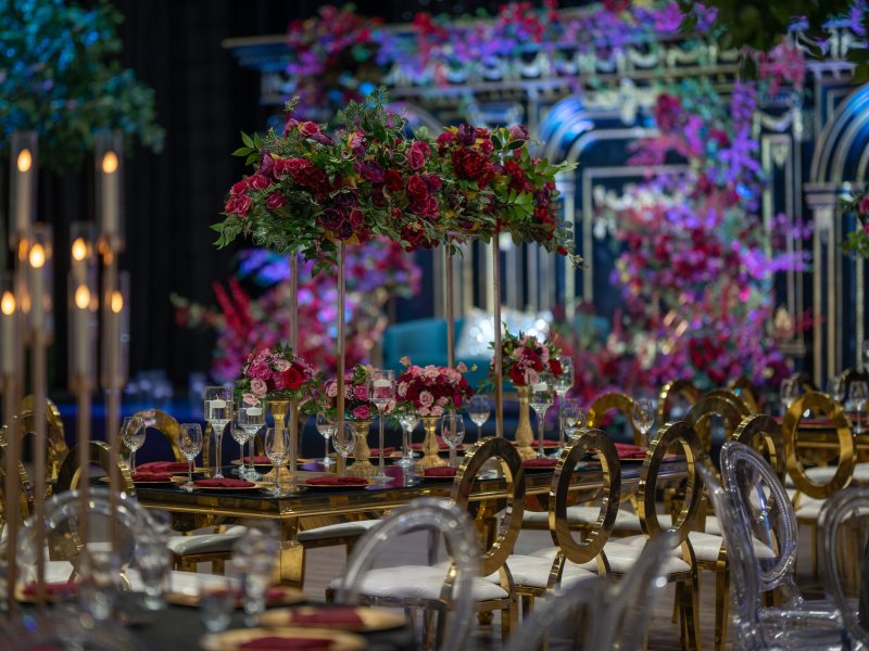 Red rose centerpiece on a gold stand with candle cylinders and gold ring-back chairs.