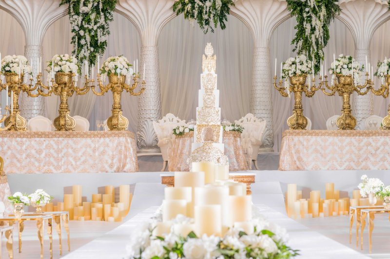 Tall white tiered wedding cake between gold candelabras with white roses, blush sequin linens and pillar candles.