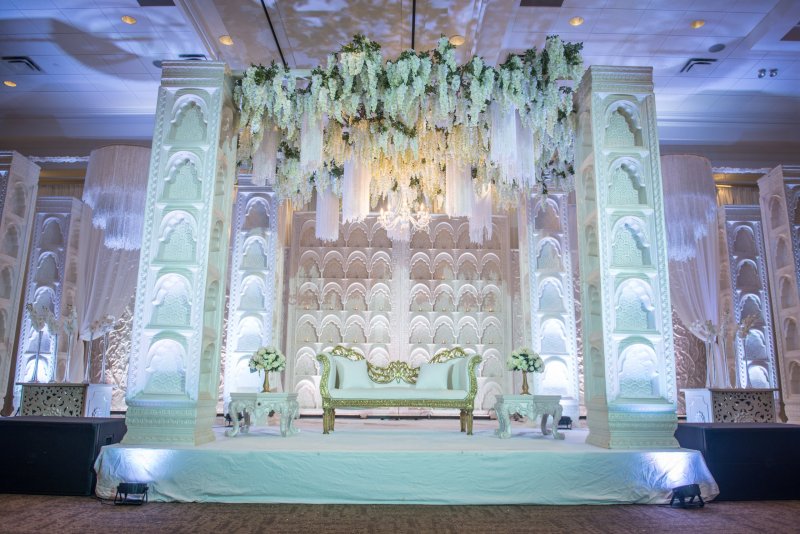 White carved pillar stage with hanging white wisteria and a gold-trimmed loveseat.