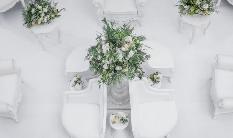 Overhead view of white lounge chairs around a table with a greenery and white flower centerpiece.