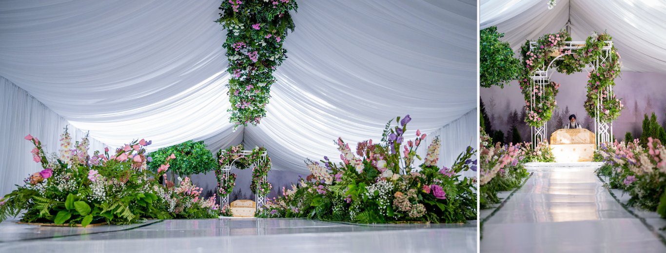 White draped tent with a hanging greenery installation, floral beds and a floral arch over a white aisle by GPS Decors