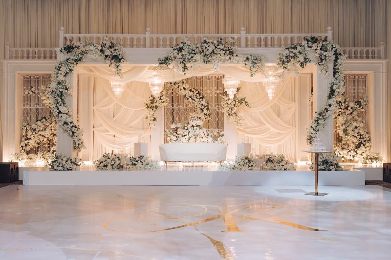 White floral arch reception stage with white drapes and a marble-look dance floor by GPS Decors