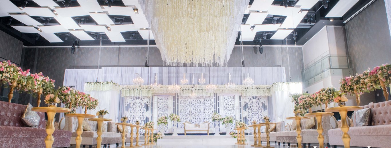 White reception with a hanging floral chandelier, pink florals on gold stands and lounge seating by GPS Decors